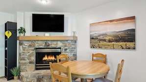 Ein Wohnzimmer mit Kamin aus Stein, einem runden Holzes Esstisch und einem flachbildfernseher, der über dem Kamin angebracht ist.