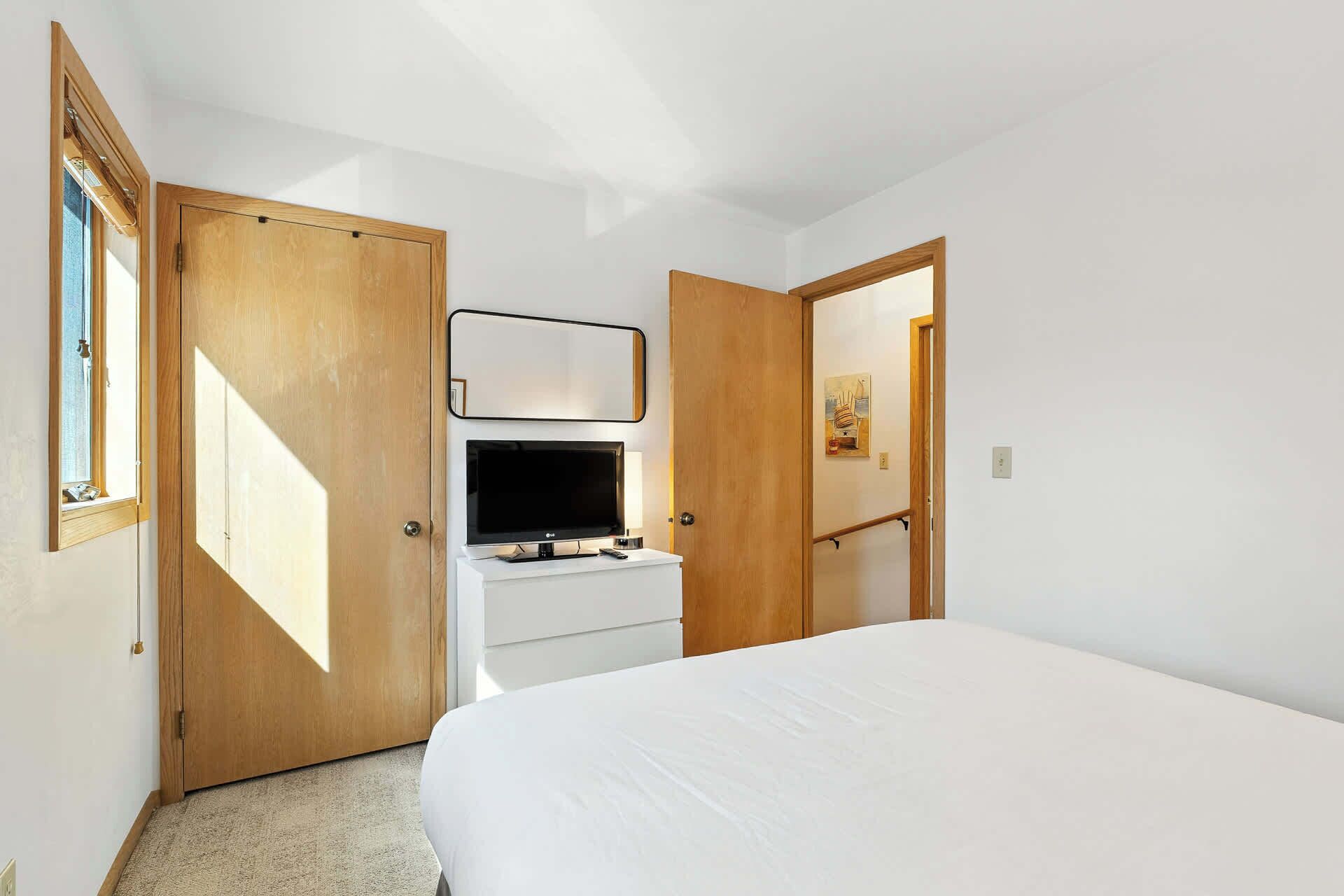 A bedroom with a bed, a TV on a dresser, and two doors.