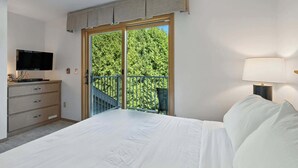 Ein Schlafzimmer mit einem Bett, einem Fernseher, einem Schminktisch, einem Balkon mit Geländer und einer Lampe.