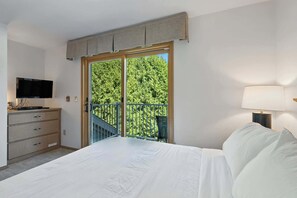 Et soveværelse med seng, fjernsyn, kommode, balkon med gelænder og en lampe.