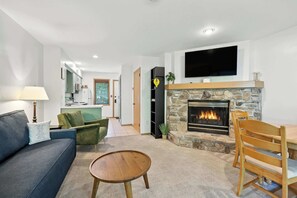 A living room with a fireplace, a television mounted above it, a sofa, a coffee table, and a dining area with chairs.