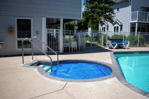 En swimmingpool med et lille spa, et overdækket område med stole og en indhegnet terrasse.