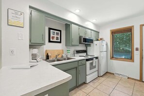 A compact kitchen with a microwave, stove, and refrigerator, a sink, and a window with a view.
