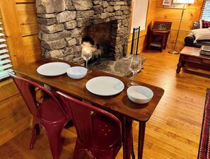 Une table à manger dressée avec des assiettes et des verres à vin, une cheminée en pierre et un plancher en bois.
