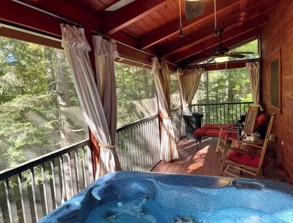 A wooden deck with a hot tub, red chairs, and curtains.