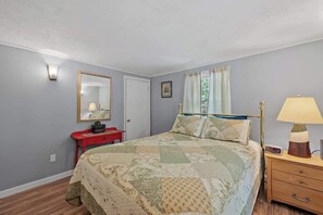 A bedroom with a bed, a nightstand, a red dresser, a mirror, and a window with curtains. - Pond Retreat: Beach, Kayak, Canoe, Deck, Firepit, (New Durham)