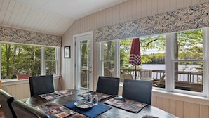 Une véranda équipée d’une table à manger, de chaises et de grandes fenêtres donnant sur un lac.