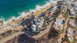 Luftaufnahme eines Küstenresorts mit Villen, einem Strand und einer felsigen Klippe.