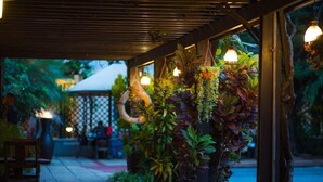 An outdoor seating area with a covered patio, hanging plants, and a view of a building in the background. - Protea Hotel by Marriott Dar es Salaam Oyster Bay (Dar es Salaam)
