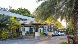 A hotel entrance with a covered walkway, palm trees, and parked cars. - Protea Hotel by Marriott Dar es Salaam Oyster Bay (Dar es Salaam)