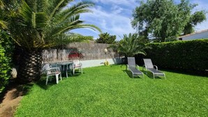 Ein Garten mit Rasen, einem Tisch mit Stühlen und einigen Liegestühlen.