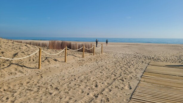 Ein Sandstrand mit einer Holzpromenade und einer Seilsperre.