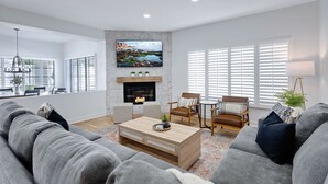 A modern living room with a fireplace, grey sofas, wooden coffee table, and a large TV mounted on the wall. - Desert Sol l Heated Pool l Hot Tub l Putting Green (Scottsdale)