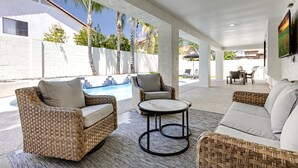 A covered outdoor area with wicker furniture, a pool, and a view of a building with a white exterior. - Desert Sol l Heated Pool l Hot Tub l Putting Green (Scottsdale)