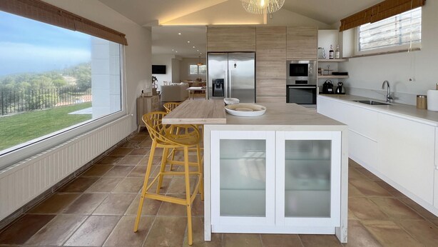 Een moderne keuken met een groot keukenblok, gele stoelen, een inbouwoven en uitzicht op de omgeving.