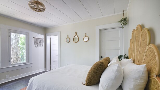 Een slaapkamer met een groot bed, wit beddengoed, een rotan hoofdbord en een hangplant.