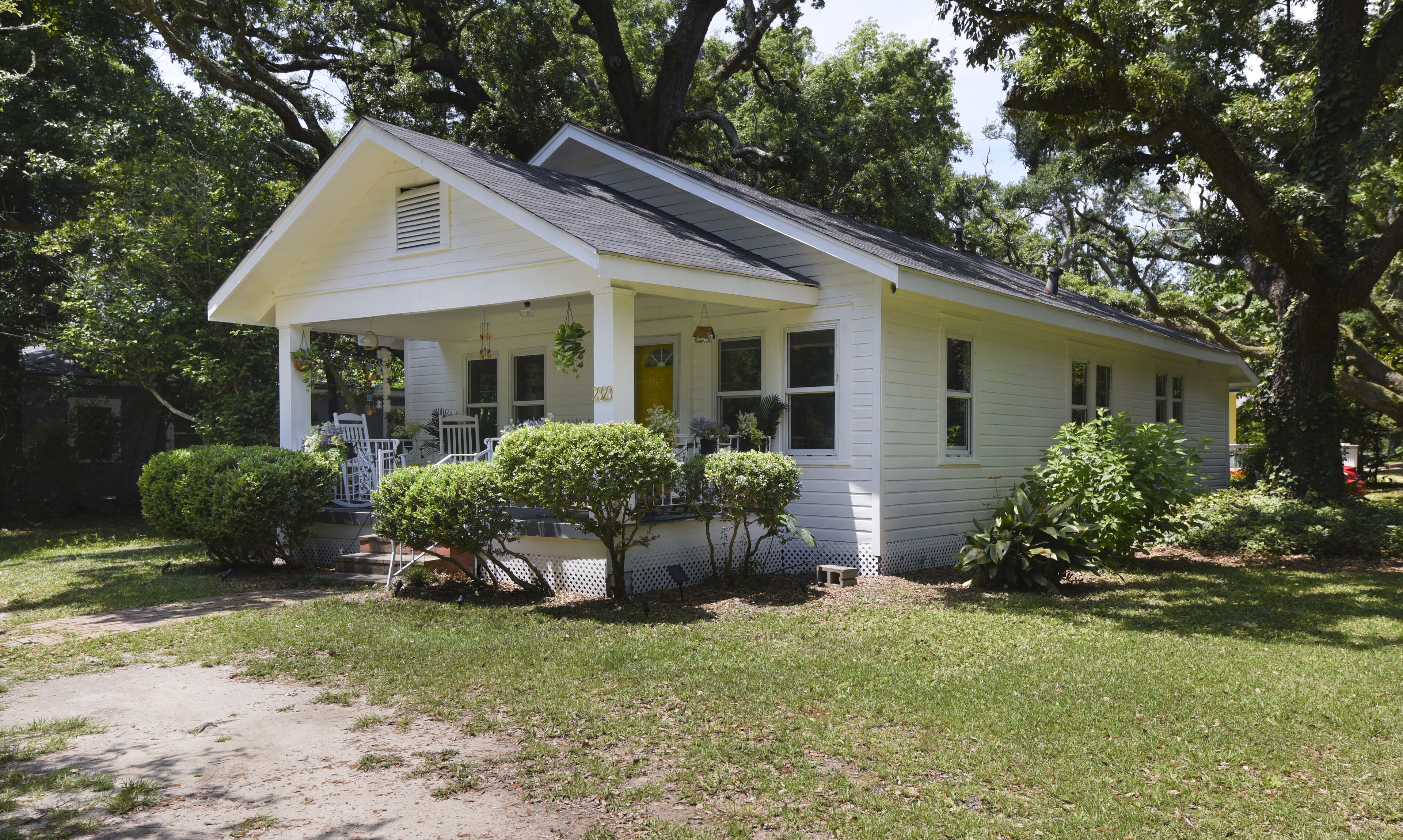 A white single-story house with a porch, surrounded by trees and a well-maintained lawn.