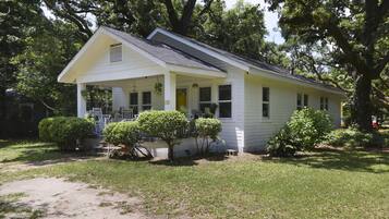 A white single-story house with a porch, surrounded by trees and a well-maintained lawn.