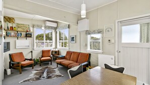 Una habitación acogedora con una mesa de madera, sillones de cuero, un sofá y una alfombra de piel de vaca. Se observan estanterías, una guitarra y una radio.