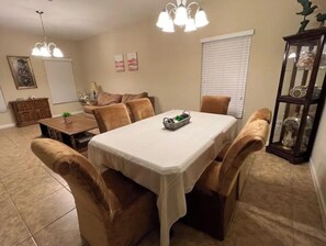 A dining area with a table and chairs, a chandelier, a cabinet with decorative items, and a window with blinds. - Florida Beach & Theme Parks, Cozy Spa & Lake Views (Rockledge)
