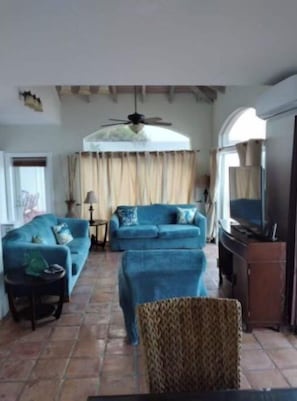 A living room with two blue sofas, a ceiling fan, a television, and a patterned chair.