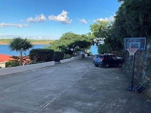 A parking area with a basketball hoop, a car, and a view of the sea.