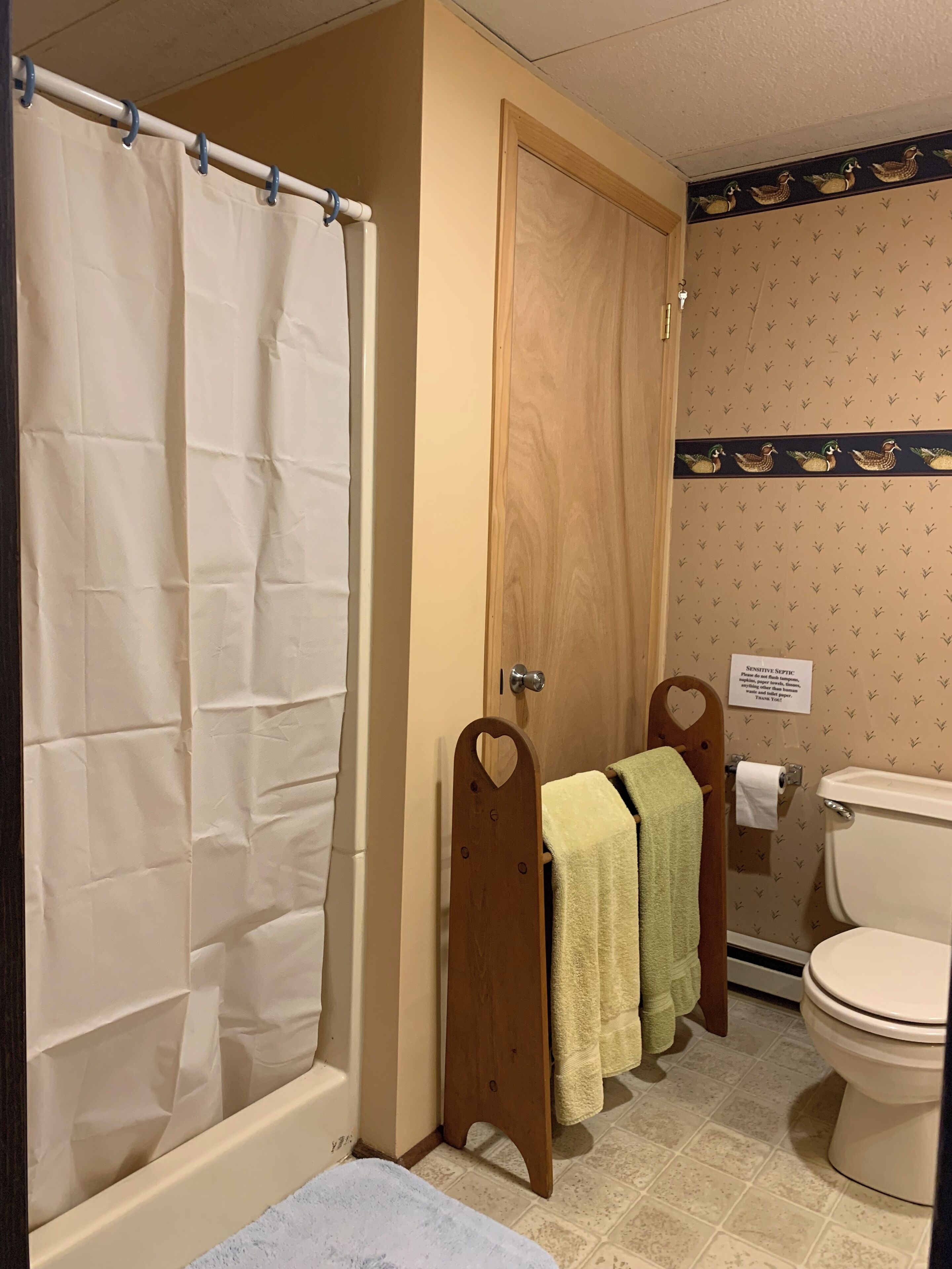 A bathroom with a shower curtain, wooden towel racks, a toilet, and patterned wallpaper.
