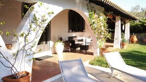 Un patio con dos sillones de relax, una mesa y una zona de estar con vistas a un jardín y un edificio con arcos.