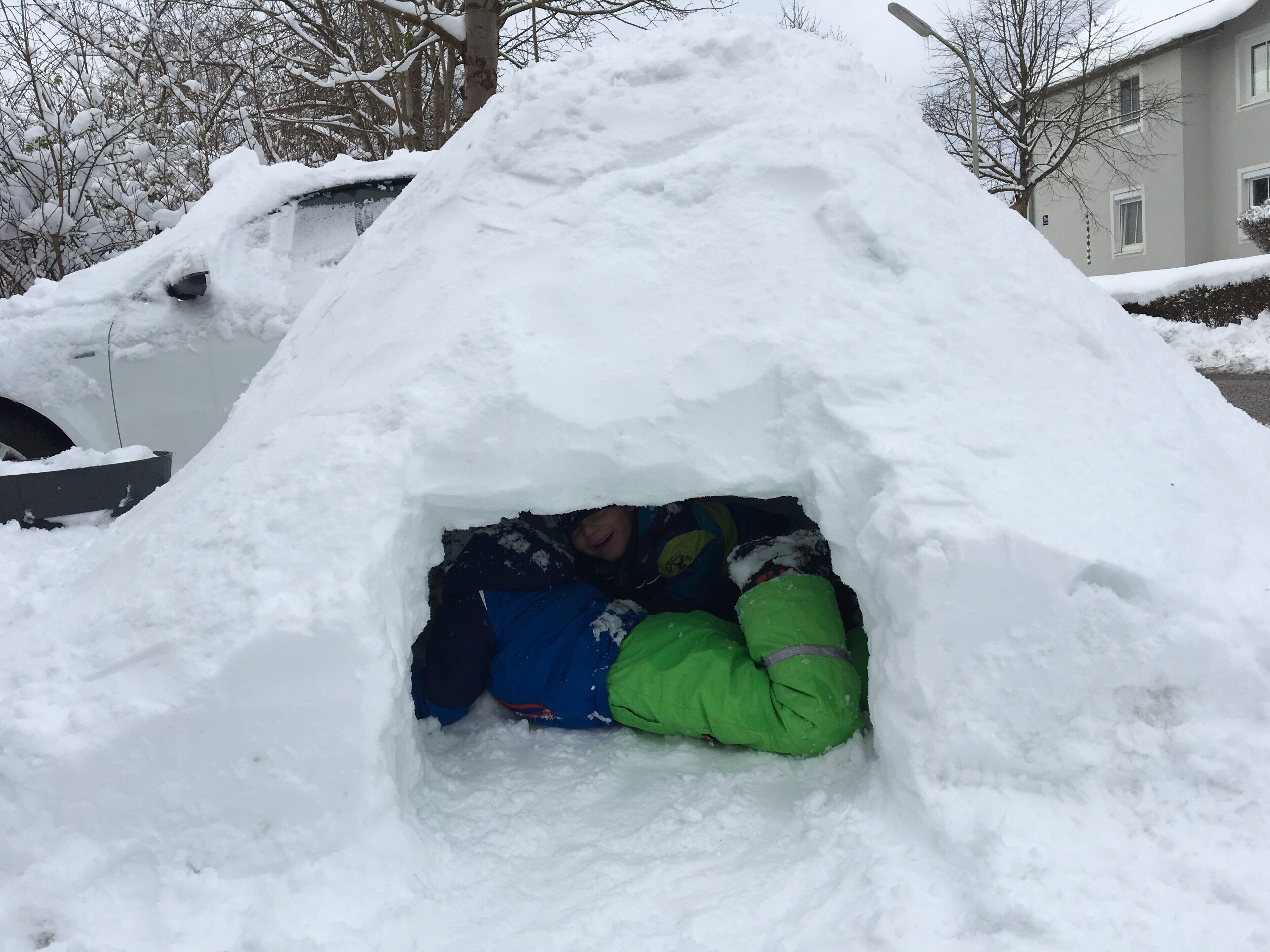 Un muñeco de nieve junto a un montículo cubierto de nieve en una zona residencial.