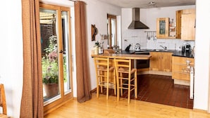 Une cuisine avec des meubles en bois, un îlot central doté de tabourets, une cuisinière et une grande fenêtre avec des rideaux.