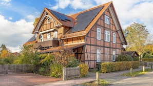 Una casa tradicional con entramado de madera, tejado inclinado, paneles solares y valla de madera.