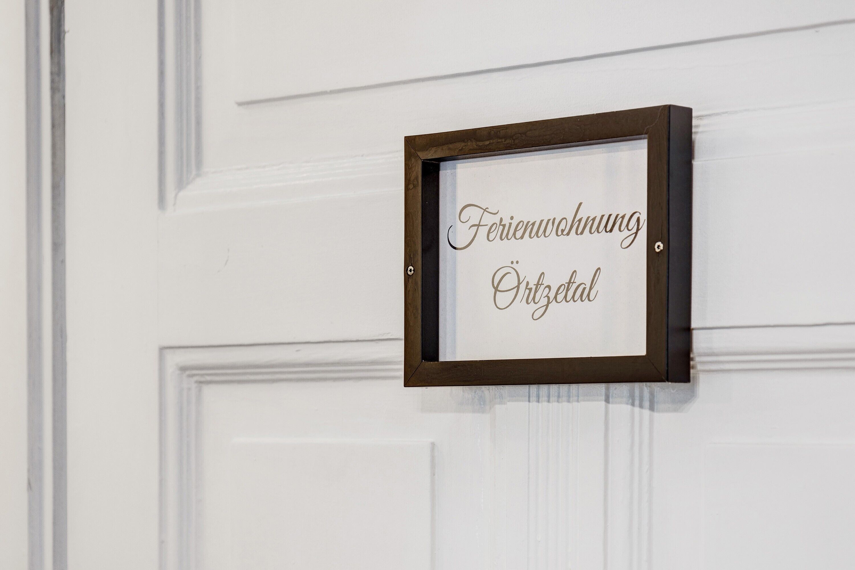 Ein gerahmtes Schild mit dem Text 'Ferienwohnung Örtzel' an einer weißen Tür.