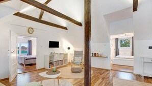 Una habitación amplia con pisos de madera, una cama, un escritorio, una silla y un televisor.