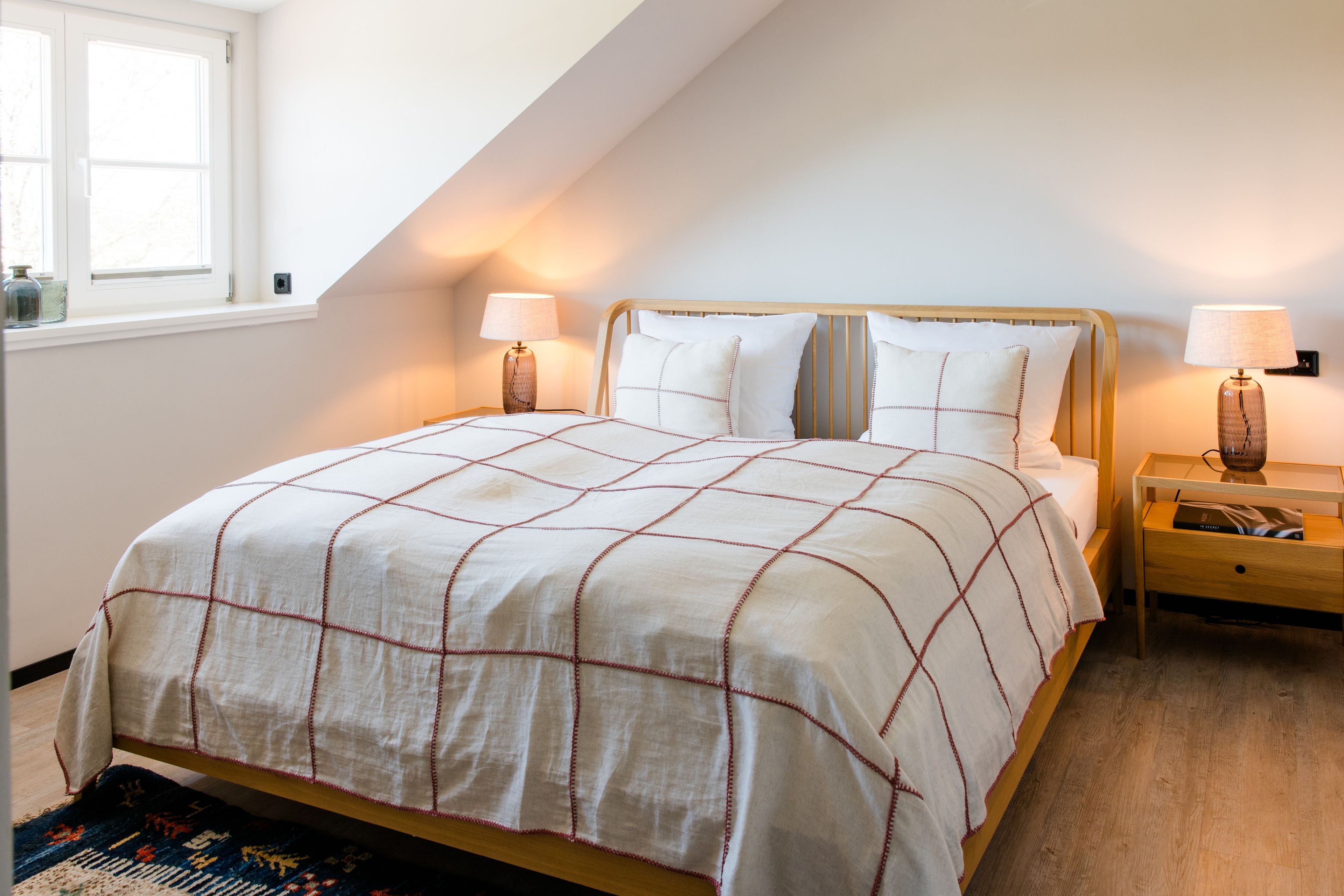 Ein Schlafzimmer mit einem Bett, zwei Nachttischen, einem Fenster und einem Schminktisch.
