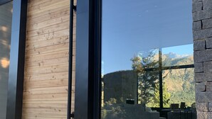 A modern building with a large wooden door, a stone wall, and a view of a mountainous landscape through large windows. - New Modern Home, Golf, Polo, Few Minutes From Catedral Ski Resort.  (San Carlos de Bariloche)