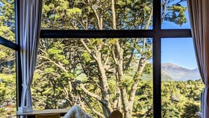 A bedroom with a large window, a bed with patterned bedding, a chair, and a small table with a fur throw. - New Modern Home, Golf, Polo, Few Minutes From Catedral Ski Resort.  (San Carlos de Bariloche)