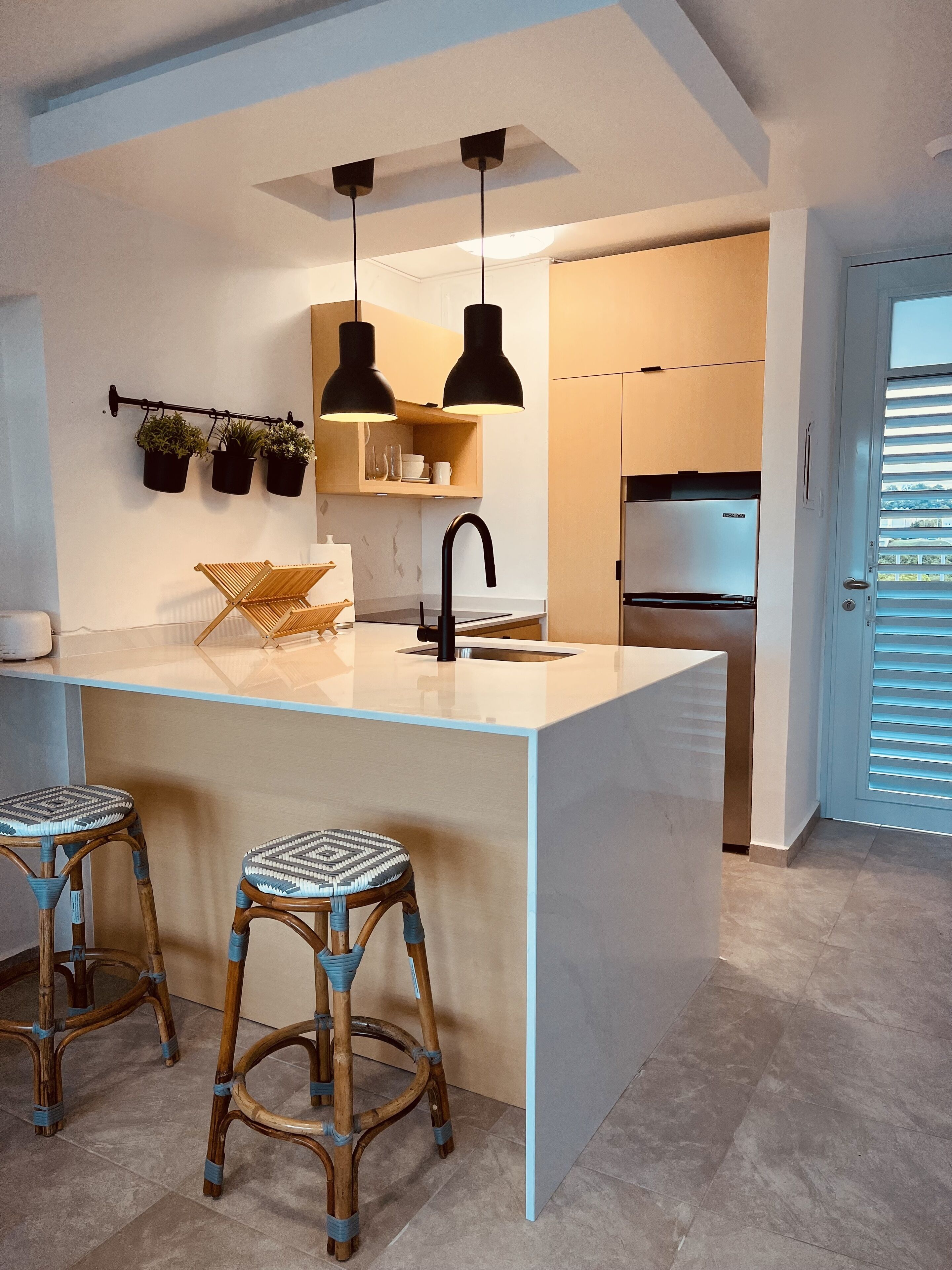 Una cocina moderna con una isla central, taburetes de bar, luces colgantes y un refrigerador empotrado.