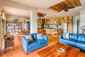 A spacious living area with two blue sofas, a wooden coffee table, and a bookshelf filled with books.