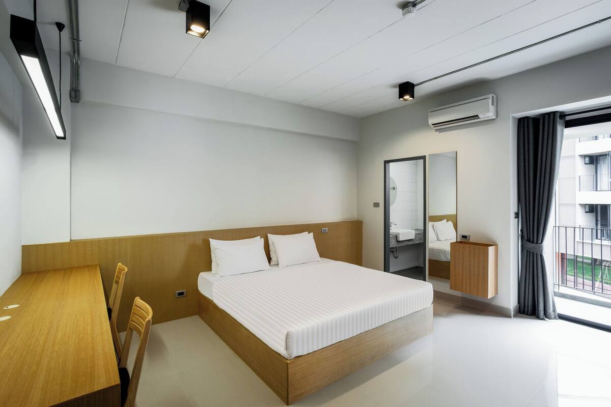 A modern hotel room with a wooden bed, a small desk, and a large window with a view of the outside.