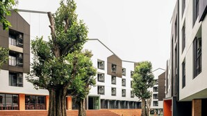 A modern building with a mix of glass and brick facades, large windows, and a central courtyard with trees and a pathway. - Raveevan Hotel At Umong (Chiang Mai)