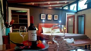 Hotelkamer met een bed, een nachtkastje met een wijnfles en glazen, en uitzicht op buiten.