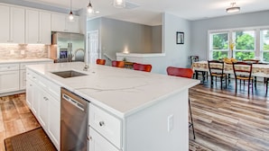 Una cocina moderna con armarios blancos, un refrigerador de acero inoxidable, una isla grande con pileta e iluminación colgante.