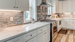 Una cocina moderna con armarios blancos, salpicadero de piedra y electrodomésticos de acero inoxidable.