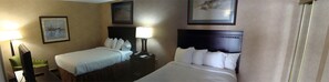 Two single beds with headboards and bedside tables, each with a lamp, are featured in this hotel room, along with framed artwork on the walls.