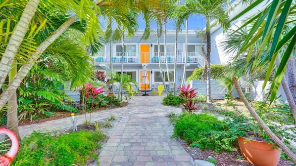 A pathway leading to a building with balconies, surrounded by tropical plants and a flamingo statue. - Beach Tide Motel - Studio 1 King bed (Hollywood)