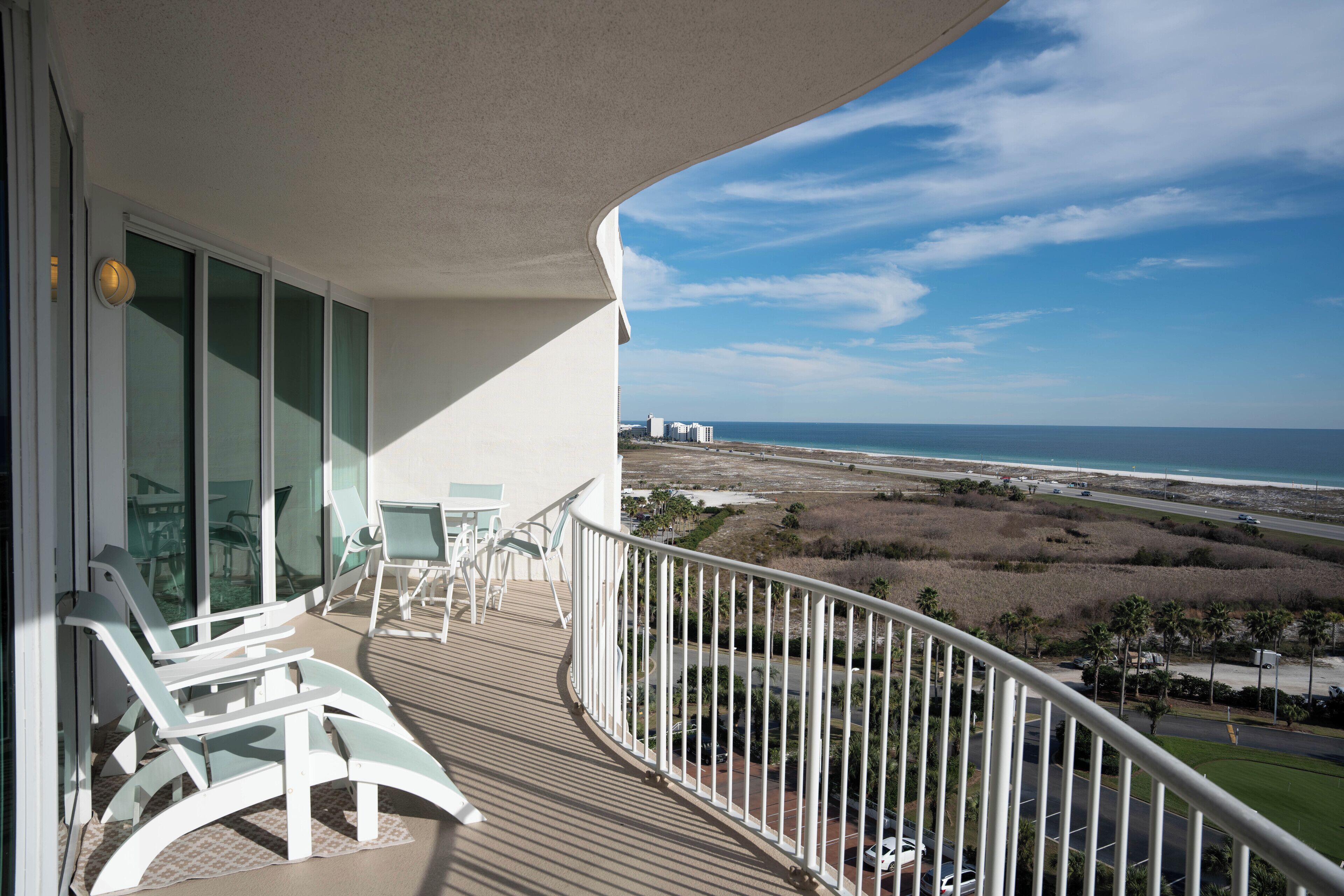 Varanda com cadeiras e mesa brancas, com vista para a praia e o oceano.