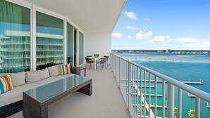 Een balkon met een bank, een tafel en stoelen, met uitzicht op een jachthaven vol boten en een helderblauwe lucht.