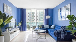 Ein modernes Wohnzimmer mit einem blauen Sofa, einem Couchtisch und einem Balkon mit Blick auf hohe Gebäude.
