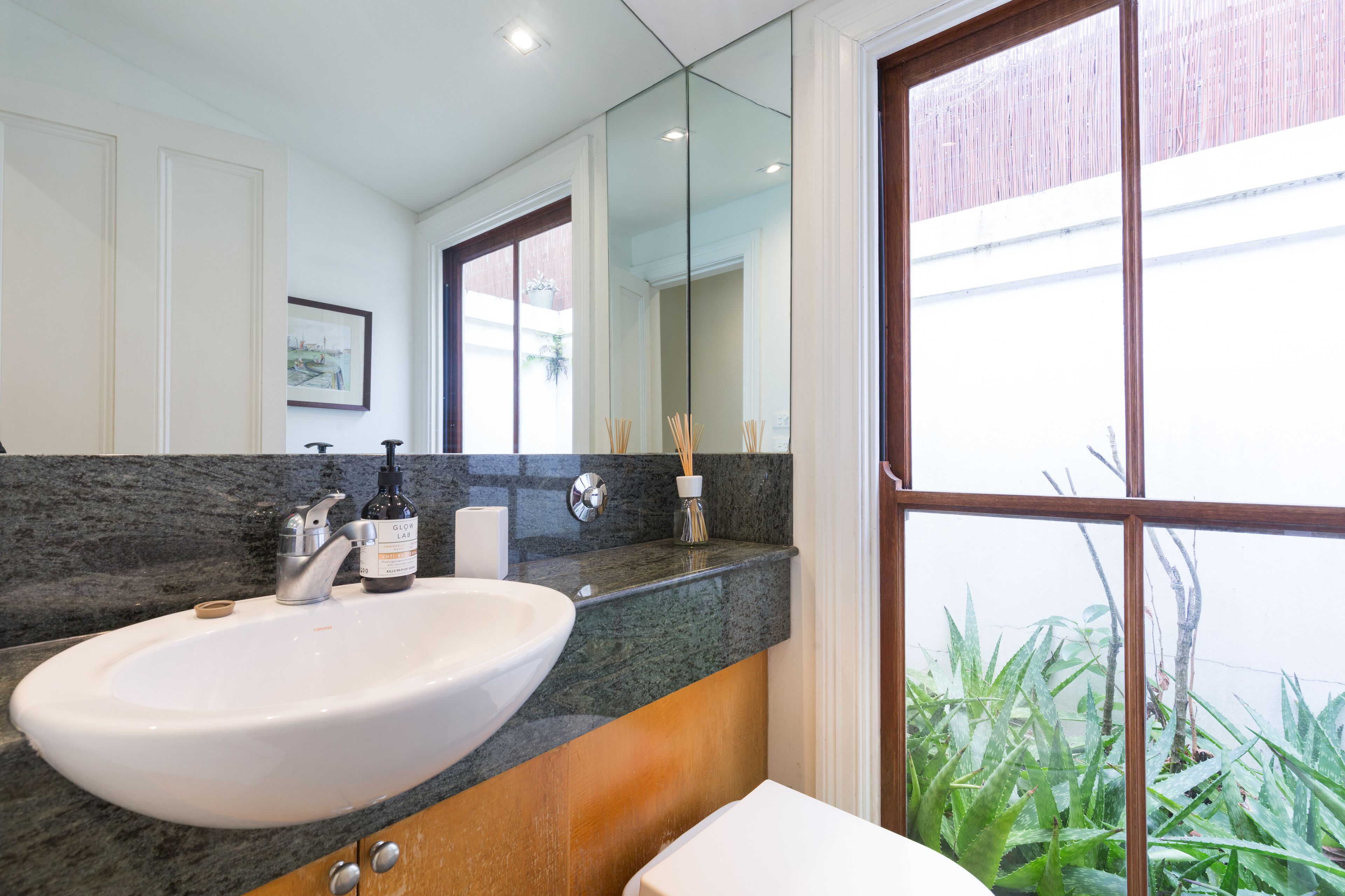 A bathroom with a large sink, a mirror, and a window with a view of greenery.