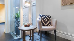 Un intérieur moderne avec une table ronde, une chaise agrémentée d’un coussin à motifs, un lampadaire et une cloison en verre ornée de plantes.